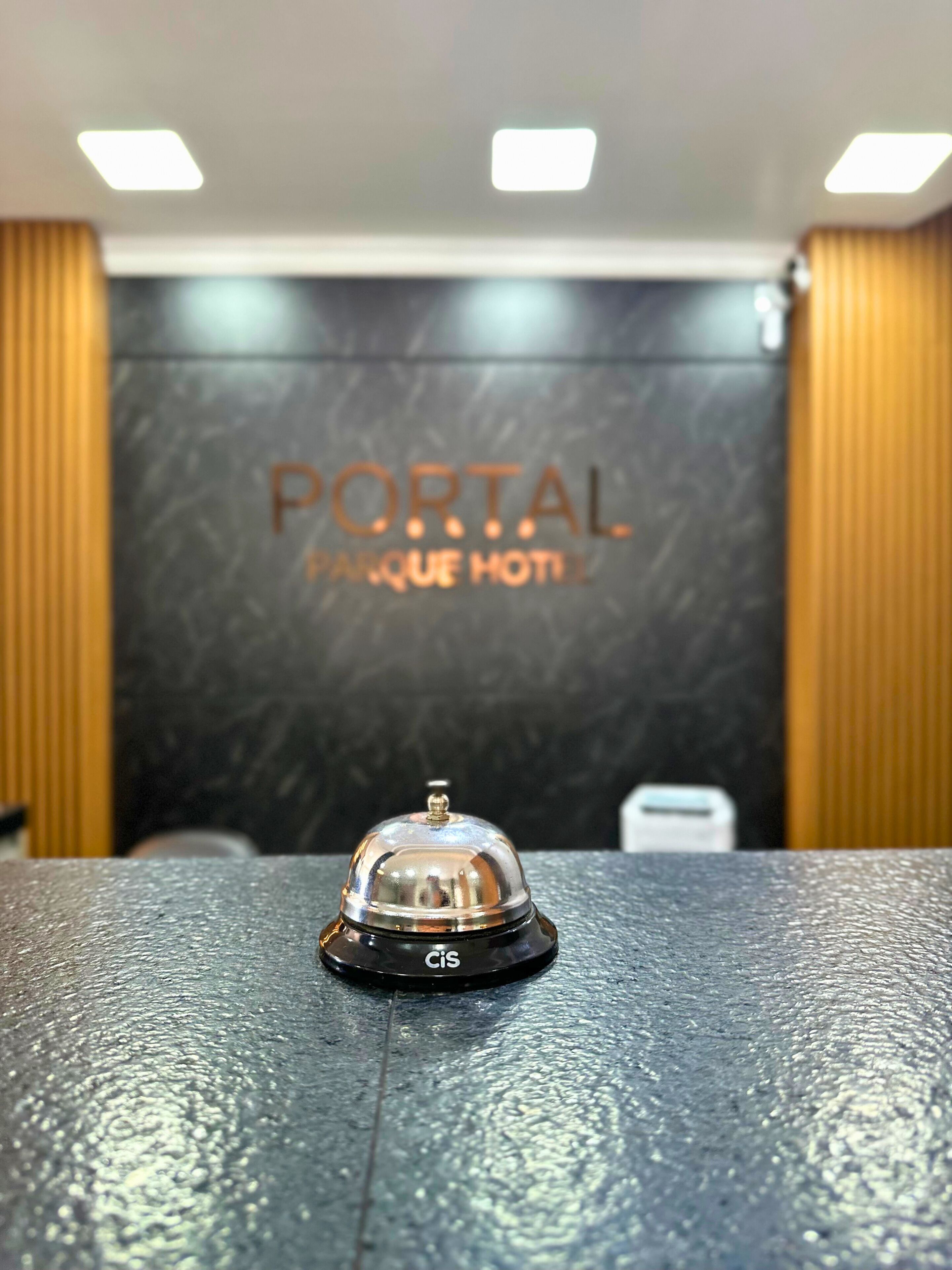 Ein Hotelrezeptionstresen mit schwarzer Struktur und einer silbernen Glocke. Im Hintergrund eine Wand mit der Aufschrift 'PORTAL UNIQUE HOTEL'.