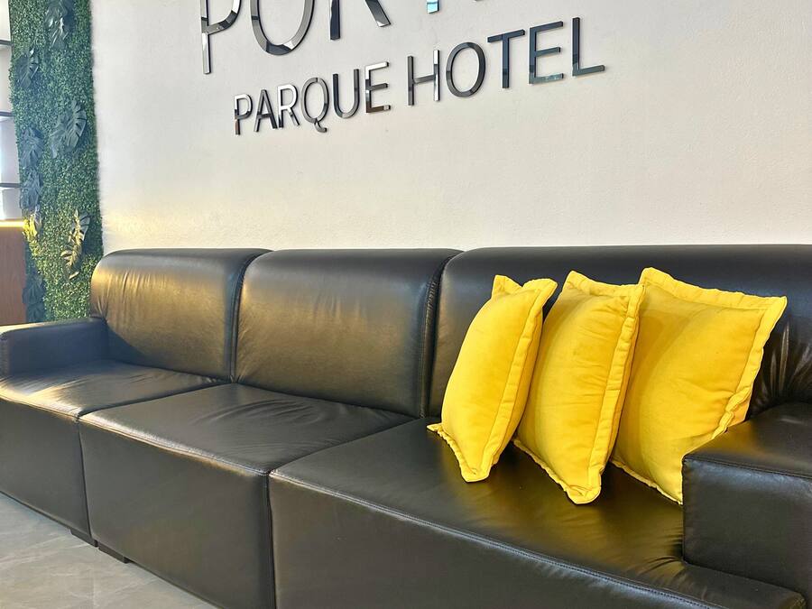 A black leather sofa with three yellow pillows in a hotel lobby with a 'PORTAL PARQUE HOTEL' sign on the wall.