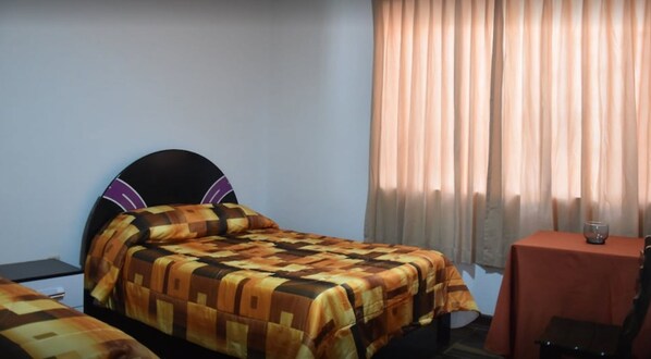 A single bed with a patterned bedspread, a bedside table with a glass, and a window with curtains. - Danys House (Cusco)