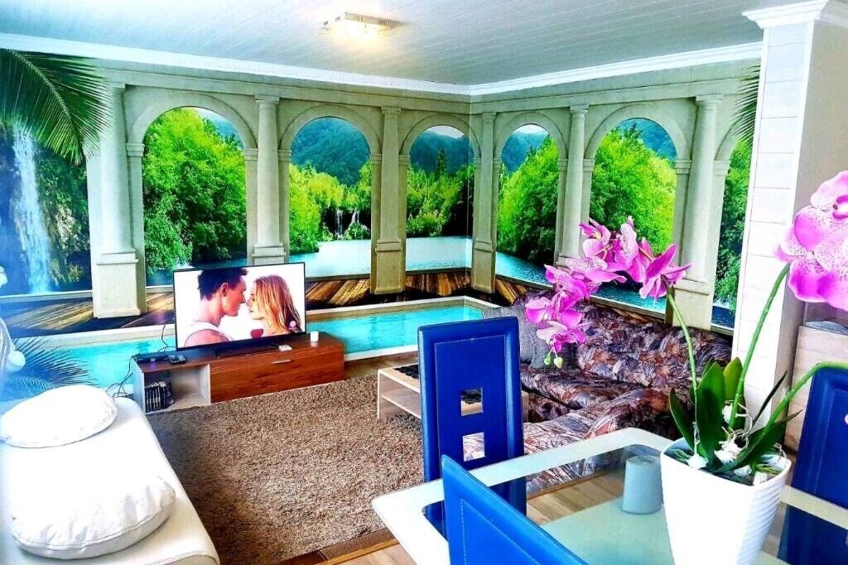 A spacious indoor area with a pool, comfortable seating, and large windows offering a view of lush greenery.