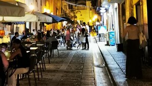 Une rue étroite bordée de cafés et de terrasses, où l’on peut voir des gens se promener et prendre leurs repas.