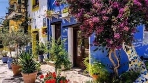 Un bâtiment à la façade bleue et au toit recouvert de tuiles, entouré de plantes et de fleurs en pot.
