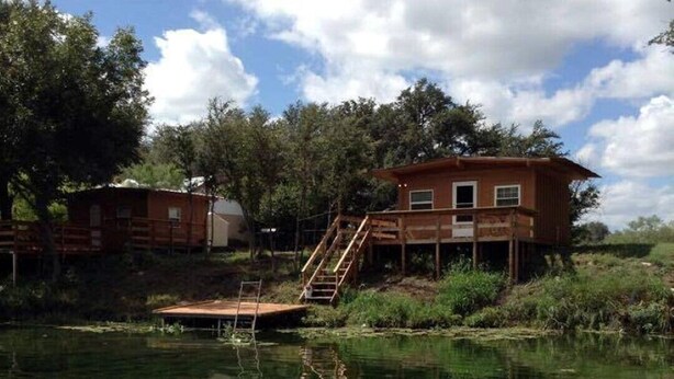 Una cabaña de madera con un muelle que se adentra en un lago, rodeada de árboles.