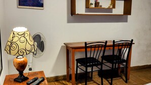 A hotel room with a bed, a desk with a chair, a lamp, a remote control, a wall-mounted shelf, and a painting on the wall. - Cozy room with private bathroom and access to kitchen with terrace in Miraflores (Lima)