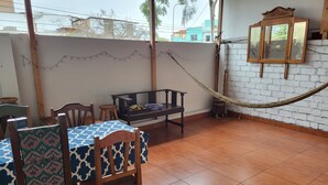 A dining area with a table and chairs, a hammock, and a wooden cabinet against a white brick wall. - Cozy room with private bathroom and access to kitchen with terrace in Miraflores (Lima)