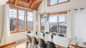 A dining area with a wooden table and chairs, large windows with mountain views, and a hanging light fixture. - 34 chemin Blanc (CITQ: 280814) (Stoneham-et-Tewkesbury)
