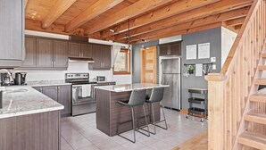 A modern kitchen with wooden beams, stainless steel appliances, and a bar area with stools. - 34 chemin Blanc (CITQ: 280814) (Stoneham-et-Tewkesbury)