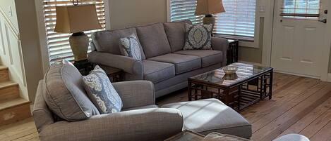 A living room with a gray sofa, two side tables with lamps, a glass coffee table, and wooden flooring.