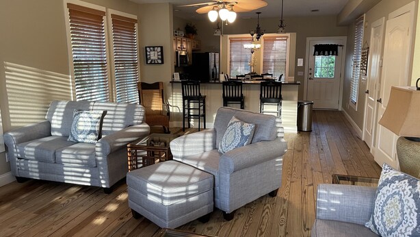 A spacious living room with a grey sectional sofa, a glass coffee table, and a wicker basket. There is a kitchen area with a bar and a dining table in the background. - Steinhatchee Landing Resort-Serendipity #48-Dog Friendly-**THIRD NIGHT FREE** (Steinhatchee)