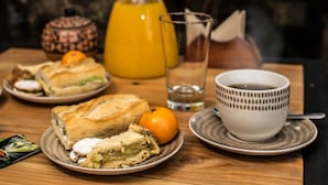 A wooden table with a plate of sandwiches, a glass of water, a cup of coffee, a glass of orange juice, and a small orange.