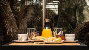 A breakfast setup with a table, plates, cups, and a juice pitcher in a forested area.