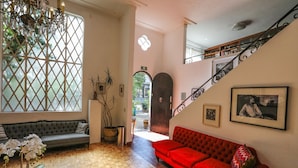 A spacious living area with a wooden parquet floor, a red sofa, a grey sofa, a glass coffee table with a plant, and a large window with a lattice design. - Hotel Casa Comtesse (Mexico City)