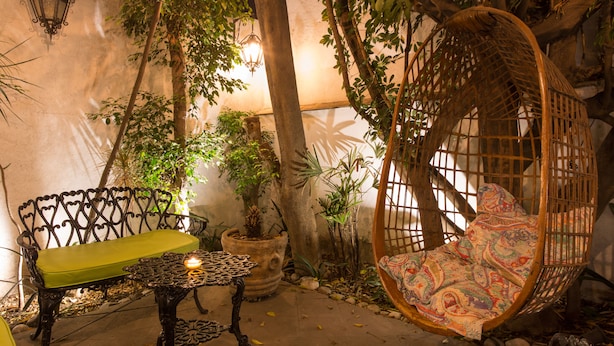 A cozy outdoor seating area with a wicker swing chair and a bench, surrounded by potted plants and trees. - Hotel Casa Comtesse (Mexico City)