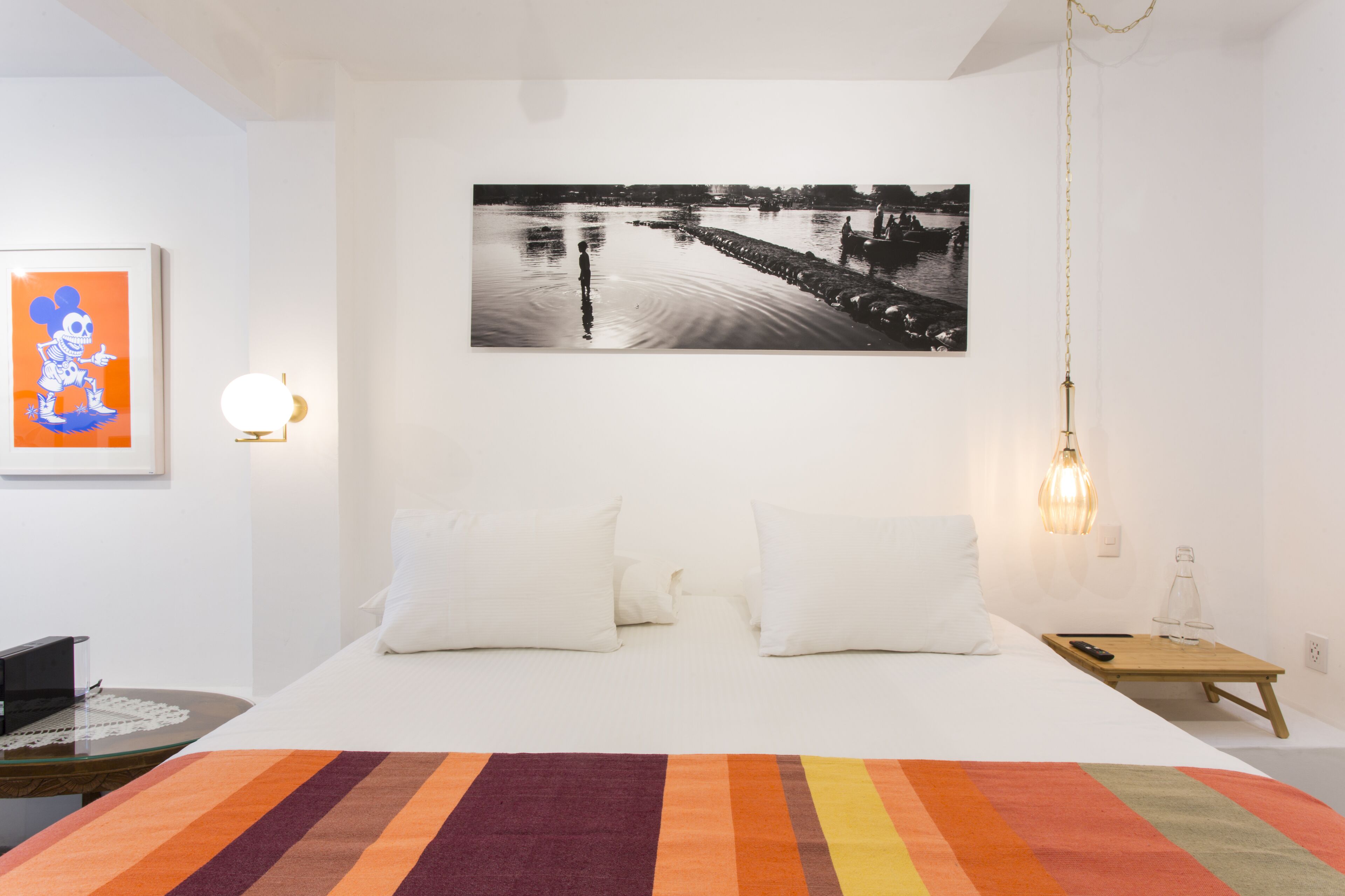 A bedroom with a bed, pillows, a nightstand, a lamp, and a framed picture on the wall.
