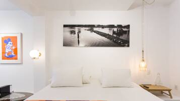 A bedroom with a bed, pillows, a nightstand, a lamp, and a framed picture on the wall.