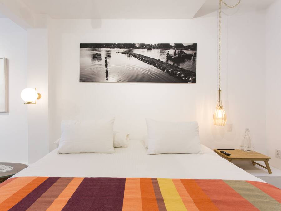 A bedroom with a bed, pillows, a nightstand, a lamp, and a framed picture on the wall.