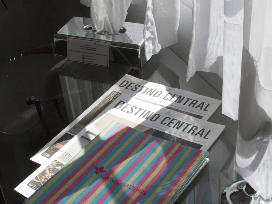 A glass table with a newspaper, a tissue box, and a striped bag on it.