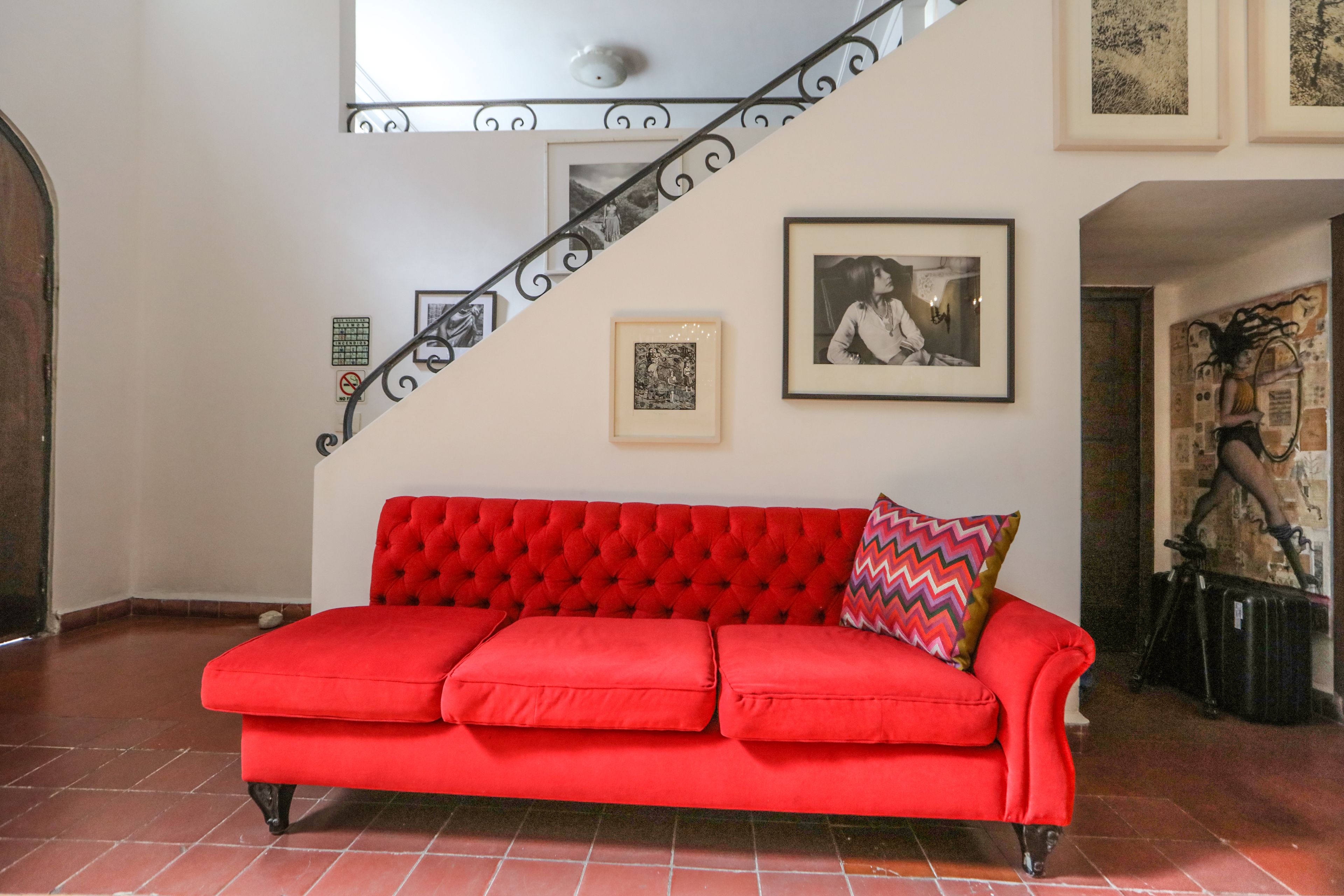 Ein rotes Sofa mit einem Zickzack-Kissen, eine Treppe mit schwarzer Geländer und gerahmte Bilder an den Wänden.