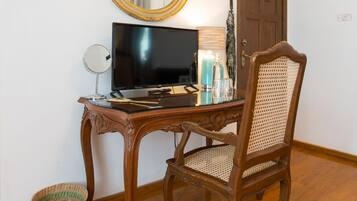 Una habitación con un escritorio de madera, un televisor, un espejo, una silla de mimbre y una puerta.