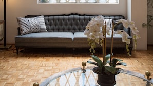 A room with a large window, a sofa, a glass table with a plant, and a chandelier. - Hotel Casa Comtesse (Mexico City)