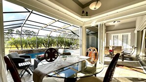 A sunlit dining area with a glass table and chairs, a view of a swimming pool, and a glass-enclosed patio.