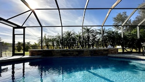 A clear blue pool with a metal roof structure, surrounded by palm trees and a stone wall.