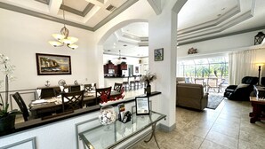A spacious hotel lobby with a glass coffee table, a dining area with a long table and chairs, and a seating area with sofas and a TV.