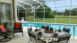 A poolside dining area with a view of a swimming pool and greenery.