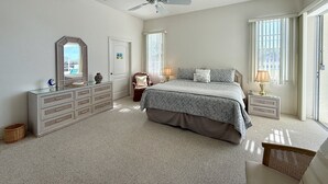 A bedroom with a bed, dresser, vanity, and a ceiling fan.