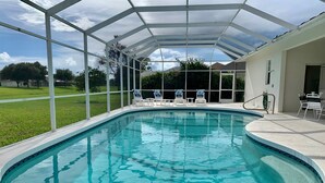 A clear, enclosed swimming pool with a glass ceiling, surrounded by a white fence and lounge chairs.