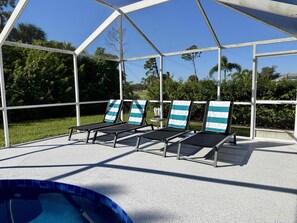 A covered outdoor area with lounge chairs and a pool.