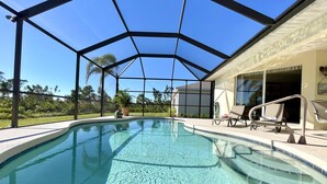 A swimming pool with a glass ceiling, surrounded by lounge chairs and a view of the outdoors.