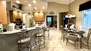 A modern kitchen with a bar area, wooden cabinets, and a dining space with metal chairs.