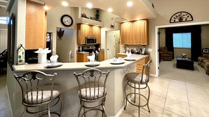 A spacious kitchen with a central island, wooden cabinets, and a microwave. There are three bar stools and a dining table with chairs.