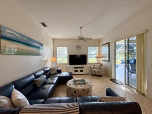 A living room with a sofa, ottoman, TV, and a ceiling fan.