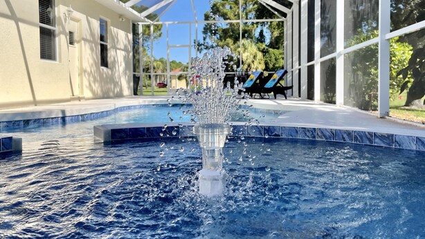 Une piscine avec une fontaine, entourée d’un espace abrité comprenant des chaises et offrant une vue sur les arbres.