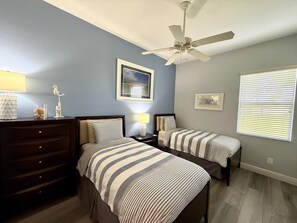 A bedroom with two beds, a dresser, a ceiling fan, and a window with blinds.