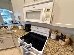 A modern kitchen with a white microwave, stove, and granite countertop.