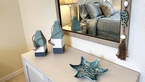 Ein Schlafzimmer mit einem Bett, einem Schminktisch, einem Spiegel und Dekorationselementen, darunter ein Seestern und zwei geometrische Skulpturen.