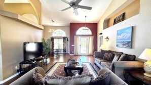 Ein geräumiges Wohnzimmer mit Deckenventilator, Fernseher, Kamin und großem Fenster.