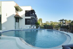 A swimming pool with lounge chairs, a building with balconies, and palm trees in the background. - Come live the barefoot dream - Your beachside paradise, and the ocean is your backyard! (Englewood)