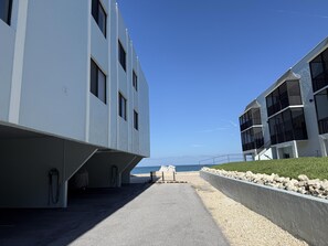 A modern building with a clear view of the ocean, a paved walkway, and a rocky shoreline. - Come live the barefoot dream - Your beachside paradise, and the ocean is your backyard! (Englewood)