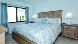 A bedroom with a large bed, wooden headboard, two bedside tables with lamps, a ceiling fan, and a window with curtains. - Come live the barefoot dream - Your beachside paradise, and the ocean is your backyard! (Englewood)