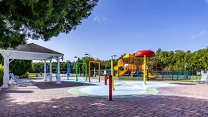 A playground with various play structures, a covered seating area, and a brick-paved ground.