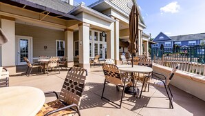 An outdoor patio area with wicker chairs and tables, a covered seating area, and a view of a building in the background.