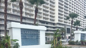 Señal para el Muelle de Lake Town con un símbolo de bicicleta, rodeado de follaje y palmeras.