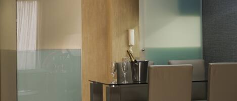 A modern hotel lobby with a glass partition, a dining area with a table and chairs, and a hanging light fixture.