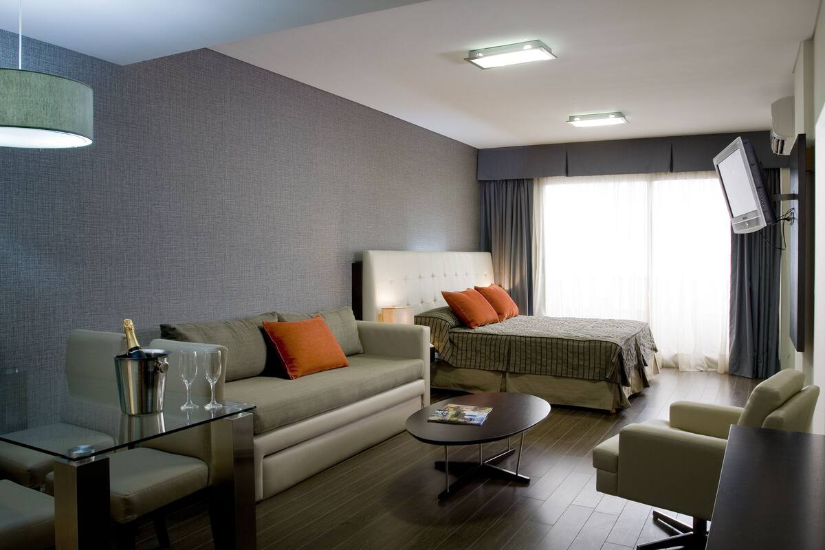 Une chambre d’hôtel moderne équipée d’un canapé, d’un lit, d’une table basse et d’un téléviseur fixé au mur.