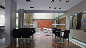 A modern interior with a wooden floor, black chairs, and tables arranged in a spacious area with a view of a red wall and a glass partition.