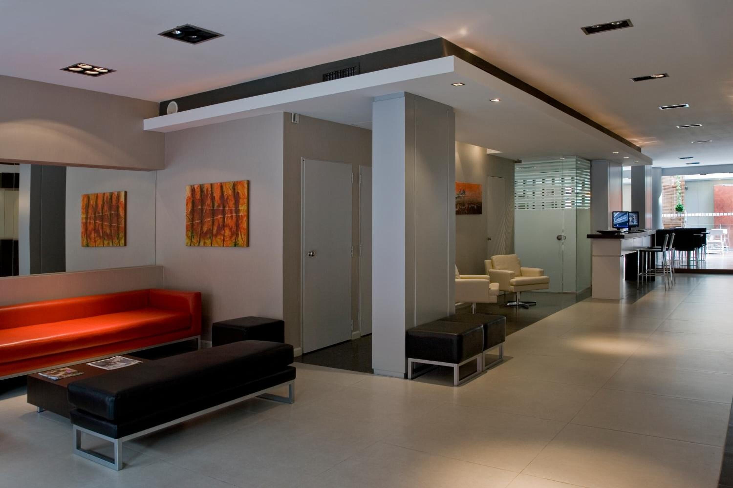 A modern hotel lobby with a red bench, black sofa, and white chairs.